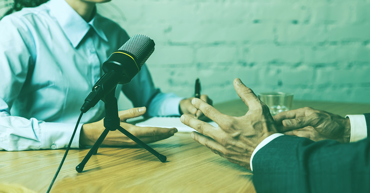 Microfono su treppiede tra due persone sedute a un tavolo durante una registrazione podcast